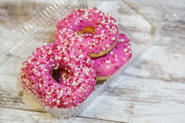 Sweet pink-glazed doughnuts in a plastic container.