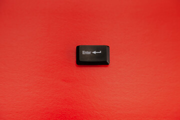 A black computer Enter key in close-up on a red background, a dangerous situation, triggering a dangerous action.