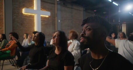 Diverse congregation singing and raising hands in worship during church service, illuminated cross...