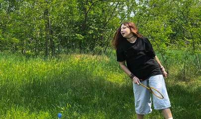 Teen girl in mid-air while playing badminton in sunny green meadow. Youth outdoor activity in summer park. Active girl enjoying outdoor activity in nature, summer lifestyle concept.