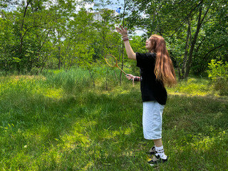 Teen girl in mid-air while playing badminton in sunny green meadow. Youth outdoor activity in summer park. Active girl enjoying outdoor activity in nature, summer lifestyle concept.