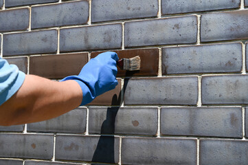 Cleaning bricks from white mineral deposits with hydrochloric acid. A worker cleans a brick wall with a brush. The result of chemical action on the building material.