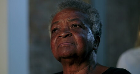 An elderly woman in the audience, with a serious expression, looking thoughtfully into the...