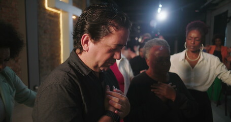 Diverse group of people with hands on chest in emotional prayer, deep connection to faith during worship session, Christian congregation, spiritual unity, cross in background