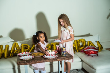 Two little girls are at a table set for a birthday party