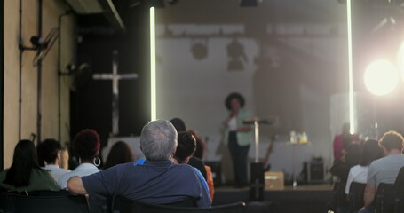 Man in the audience sitting with his back to the speaker, paying attention to a woman giving a...
