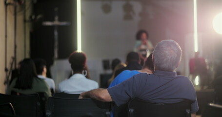 Man in the audience sitting with his back to the speaker, paying attention to a woman giving a...