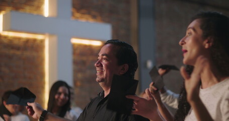 Man of Hispanic descent raising offering envelope in church worship, smiling with joy, illuminated cross in background, diverse congregation in spiritual celebration and unity