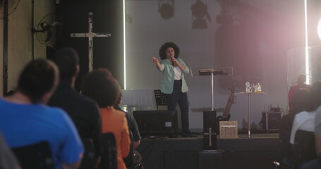 Woman passionately speaking at a church event, addressing the audience with a microphone, cross in...