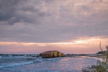 A stunning sunset casts a warm glow over the serene waters of Zakynthos, highlighting the remnants of an ancient structure by the shore
