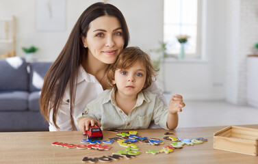 Fototapeta premium Mother, young babysitter and little child playing logic strategy wooden board game at table together, caring mom teaching kid boy, happy family engaged in educational activity at home, learning 