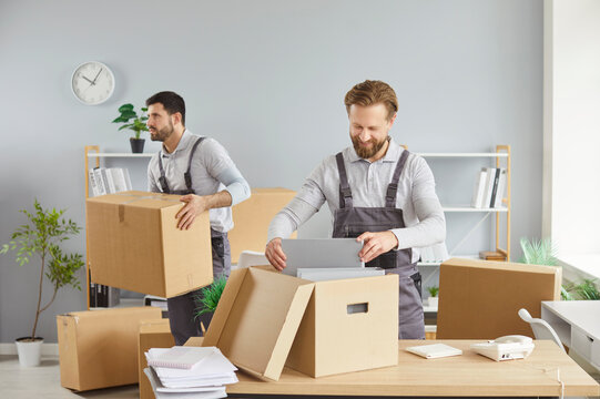 Moving delivery pack service, male movers team moving cardboard boxes, loading, unloading setting up of household goods, new house stuff, carrying stacks of cardboard relocation boxes in office room