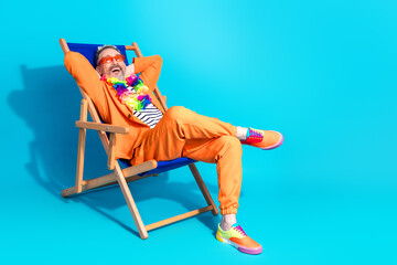 Charismatic mature man in vibrant orange attire enjoying relaxation in a deck chair on a colorful...