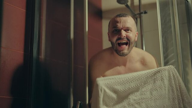 A man dries himself with a towel in the shower.Video portrait face young European happy man taking relaxing shower at home.