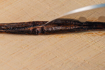 Vanilla bean cut open with a kitchen knife on a wooden cutting board 
