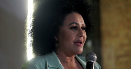 Close-up of a woman speaking passionately into a microphone during a spiritual event, confident...