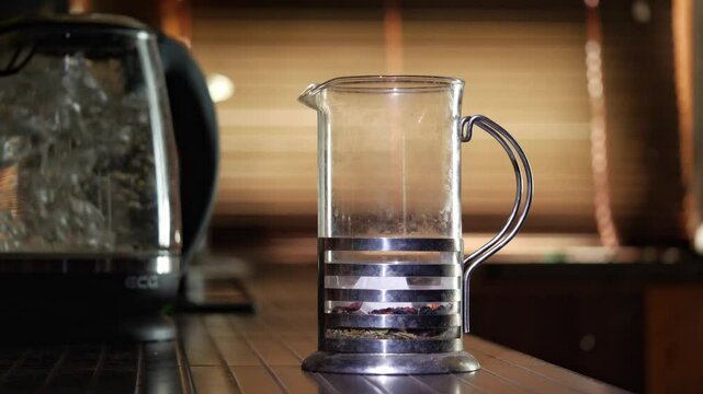 A close-up shot captures the calming mood as hot water is poured from a kettle into a French press filled with loose leaf tea, showing the brewing process in a warm, inviting setting