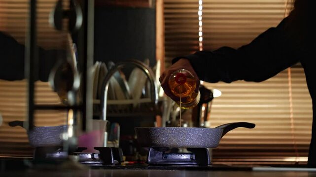 A mid-shot captures a warm, domestic mood as a hand pours cooking oil from a bottle into a pan on a gas stove, highlighting the start of cooking in a kitchen setting