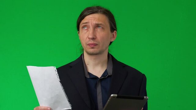 A mid-shot captures the tired and frustrated mood of a man holding a digital tablet, resting his hand on his cheek, against a vibrant green screen, ideal for customizable backdrops