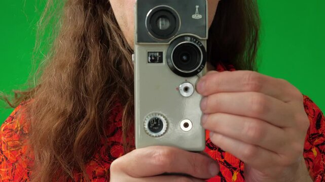 A close-up shot captures an engaged and focused mood as a man's hands adjust the settings on a vintage film camera, with his face partially visible behind it, against a green screen