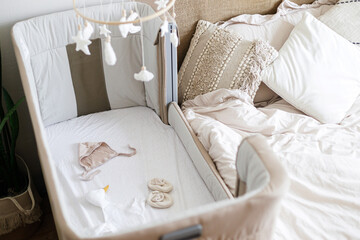 Modern baby crib with stylish baby clothes, toy, boho mobile, comforter. Pregnancy and getting...