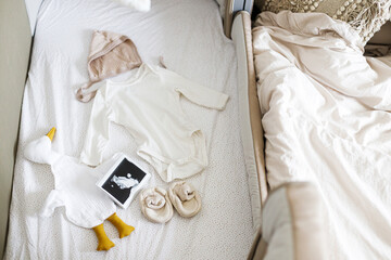 Pregnancy and getting ready for baby, top view. Modern baby crib with stylish baby clothes, toy, boho mobile, ultrasound picture.Preparation and making nursery