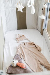 Pregnancy and getting ready for baby. Stylish baby clothes, toy, comforter in modern baby crib, close up. Preparation and making nursery