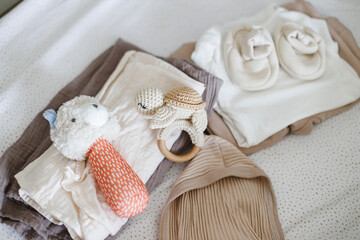 Stylish baby clothes, toy, comforter in modern baby crib, top view. Pregnancy and getting ready for baby. Preparation and making nursery