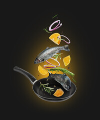Sea trout with rosemary branches and lemon slices falling into frying pan on black background