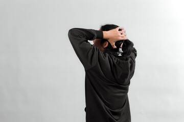 Rear side portrait of an Asian young person holding head with both hands, expressing stress or...