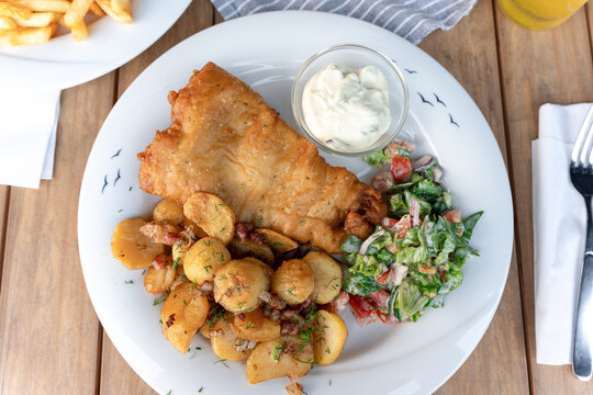 Teller mit frischem Backfisch, Bratkartoffeln und Salat

