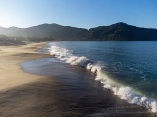 The sun shines on a beautiful morning on the beach with orange sand and strong waves
