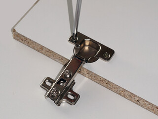 Installing a furniture door hinge, close-up of a screwdriver screwing in a furniture hinge