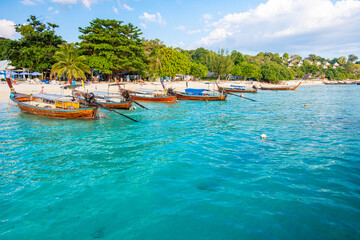 Crystal clear turquoise water gently laps the shore of Long Beach in Phi Phi Don, Thailand, where traditional longtail boats are moored, creating a serene and picturesque scene