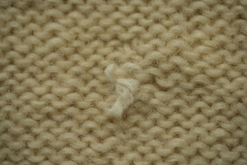 beige knitted fabric showing detailed fibers, stitches, and a small thread knot. The soft texture and warm color make it suitable for backgrounds, textile themes, craft projects, knitting, fashion, se