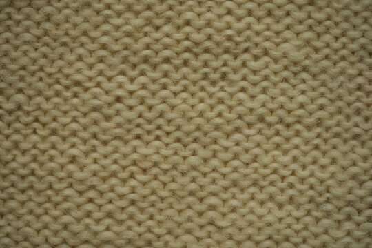 macro texture of white wool knitted fabric. Handcrafted with knitting needles, the soft yarn forms a cozy and natural background. Ideal for textile design, winter themes, handmade crafts, or slow fash