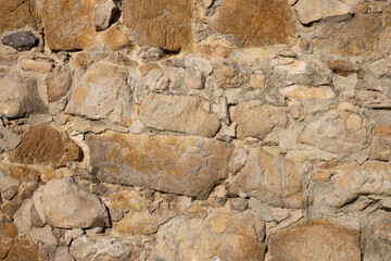 Old rustic wall made of beige and ochre stones

