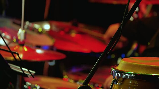 Close-up of a drummer playing at a concert against a backdrop of congas. The setup and the musician's hands are blurred. Slow motion