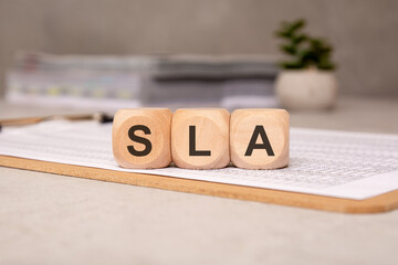wooden cubes spelling SLA on a clipboard with documents, symbolizing service-level agreement