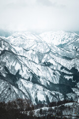 Obraz premium A breathtaking panoramic view of snow-covered mountain ranges including Ishiuchi Maruyama, Yuzawa Kogen, and distant peaks near Echigo-Yuzawa in Niigata, Japan, captured from Gala Yuzawa station.