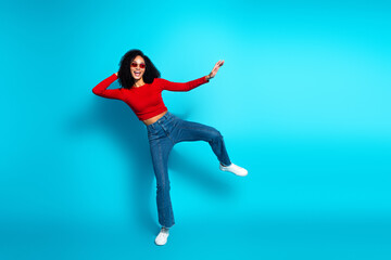 Stylish young woman in red top dancing joyfully on a vibrant blue background