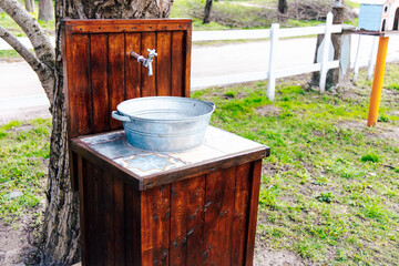 Rustic outdoor wash station with water faucet and metal basin beside a gravel path