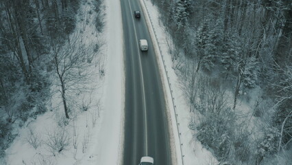 Aerial view of a winding snowy mountain road cutting through a dense winter forest. Mountain road...