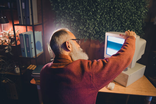 Senior man concentrating on an old computer screen in a cozy office environment during an evening light setting