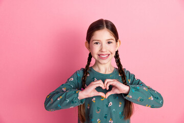 Charming young girl making heart gesture with hands, wearing casual outfit, smiling with happiness...