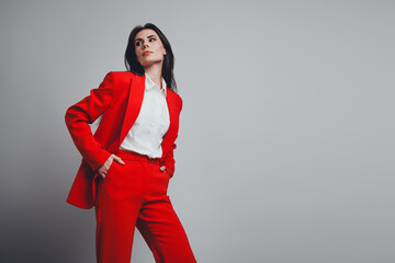 Confident businesswoman in a bold red suit posing against a modern gray background with a trendy...