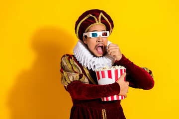 A young man wearing a royal outfit eating popcorn and enjoying a 3D movie against a vibrant yellow background