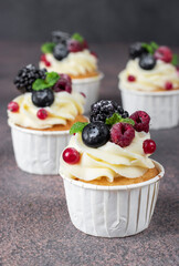 Homemade cupcakes decorated with cream cheese and berries on brown background