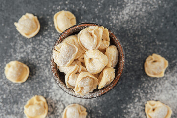 Homemade cappelletti pasta in wooden bowl with scattered pieces on table