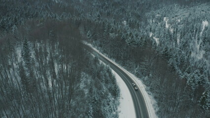 Aerial view of a winding snowy mountain road cutting through a dense winter forest. Mountain road...